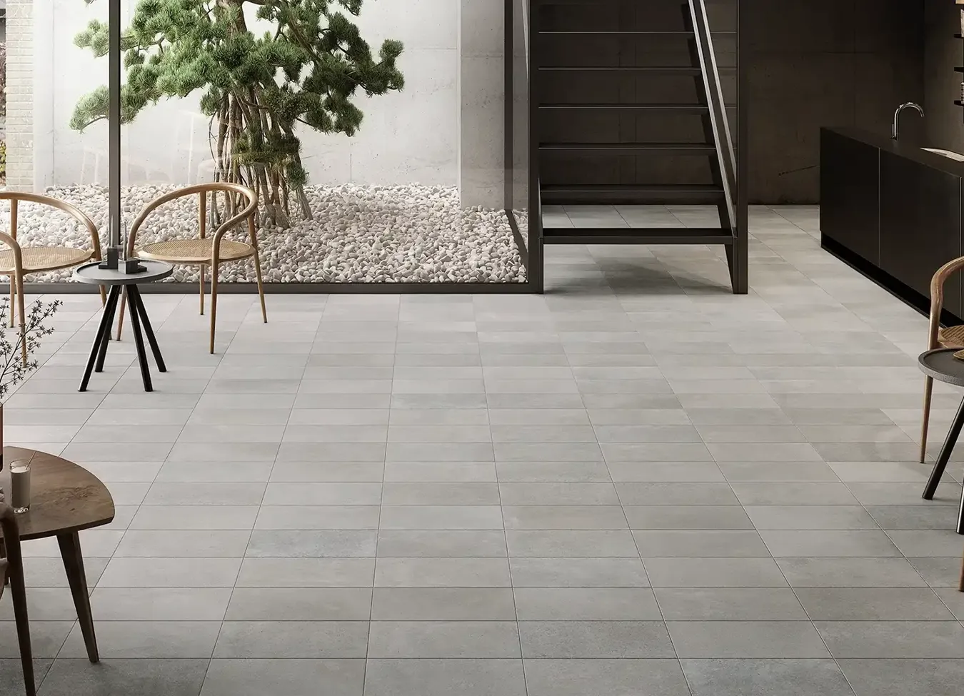 Pavimento in gres porcellanato grigio in spazio architettonico intergenerazionale con scala e giardino zen
