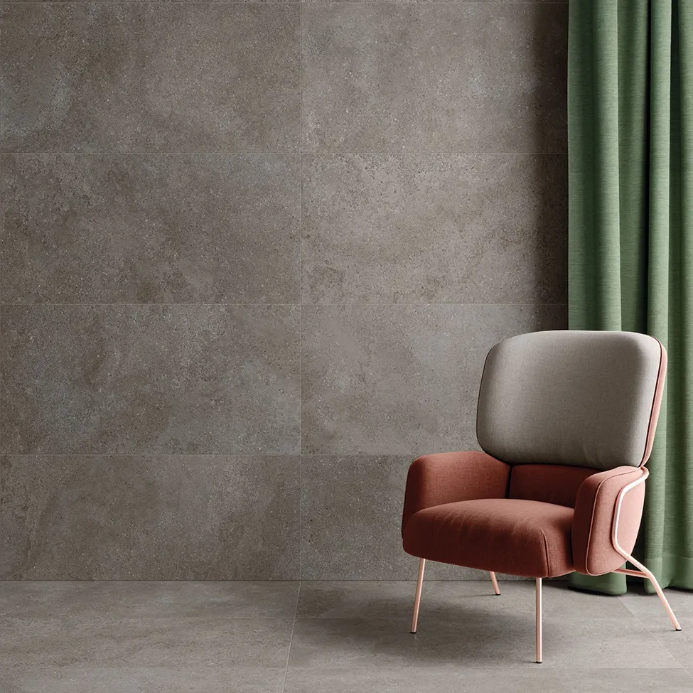 Revêtement mural en grès cérame effet pierre calcaire taupe dans un salon avec fauteuil terracotta et rideau en lin vert