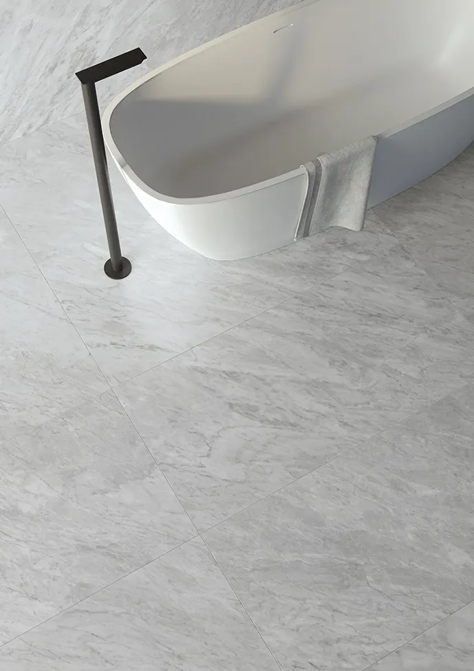 Suelo de gres porcelánico efecto mármol con acabado sedoso en un baño con bañera exenta que resalta la superficie lisa y satinada