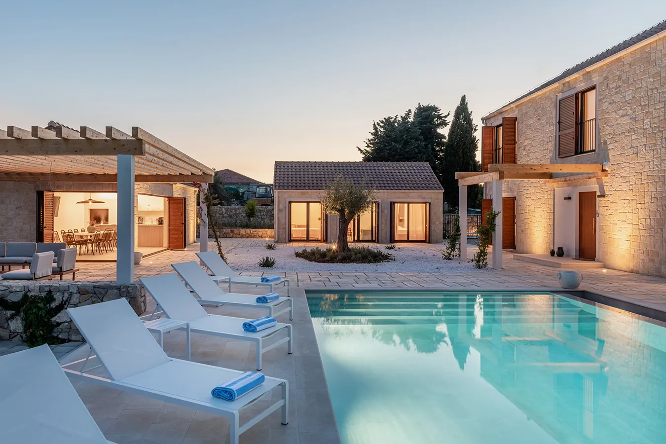 Heat-resistant, light ivory concrete-effect porcelain pavers around an outdoor pool at dusk