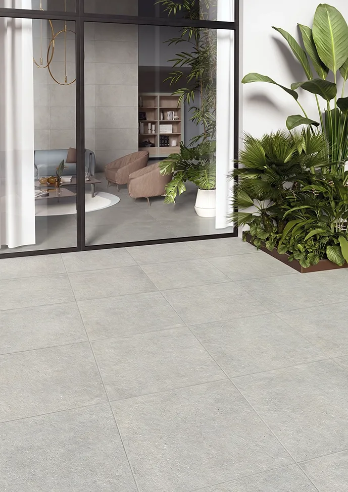 Dalles en grès cérame effet béton gris sur une terrasse intérieure-extérieure avec mobilier lounge et végétation