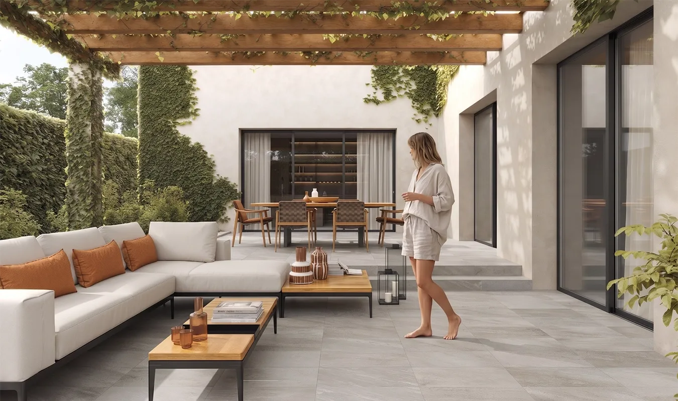 Femme marchant pieds nus sur des dalles en grès cérame extérieur Point Silver, sur une terrasse couverte d'une pergola avec salon et coin repas extérieurs