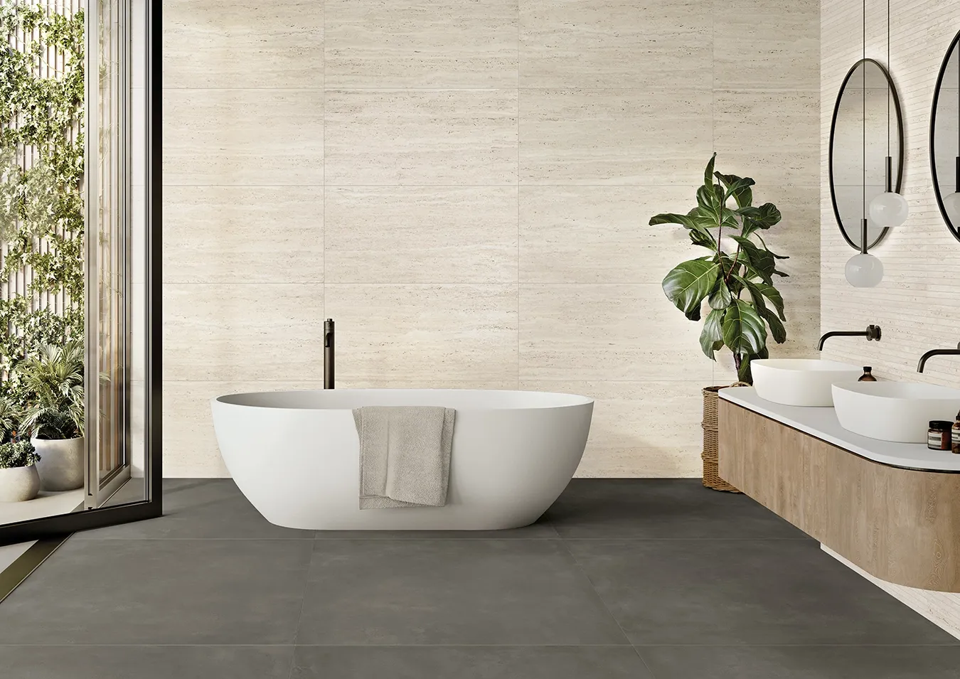 Bagno con rivestimento in grandi lastre effetto travertino avorio a tutta altezza, vasca freestanding e pavimento scuro