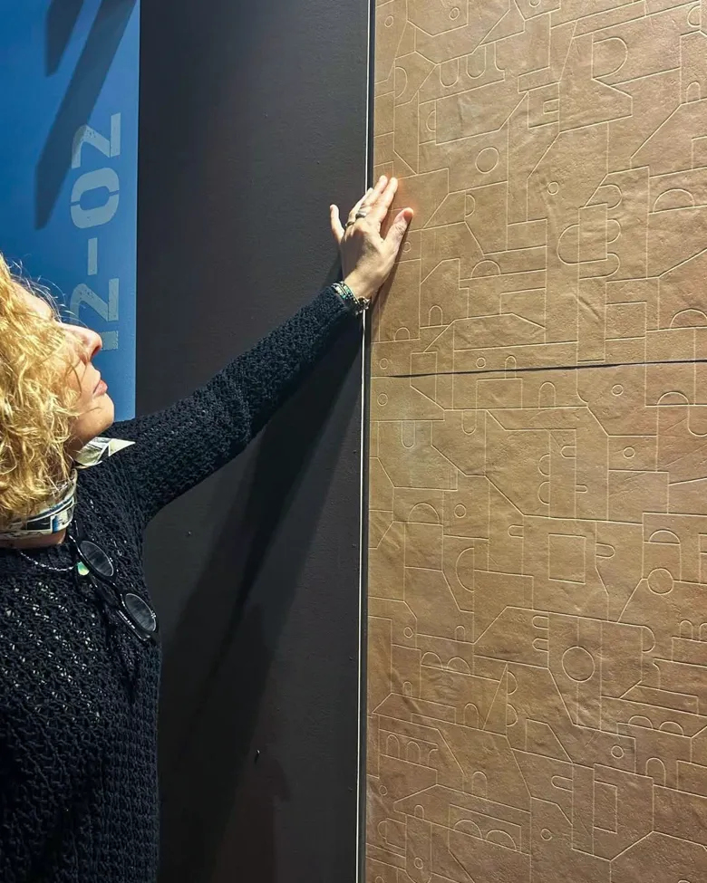 Person berührt ein Feinsteinzeugpaneel mit Reliefdekor in Terrakottaoptik, Installation SaloneSatellite 2026.