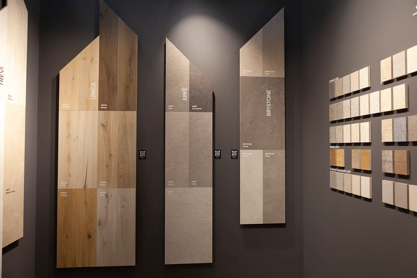 Vertical wall displays showcasing wood-look and stone-look porcelain stoneware tiles from the Unica, Arkè, and Brystone collections.